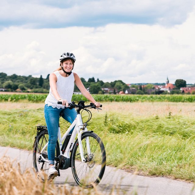 Eine Frau mit einem schwarzen Fahrradhelm sitzt auf einem Mountainbike und lächelt vor einer Blumenwiese