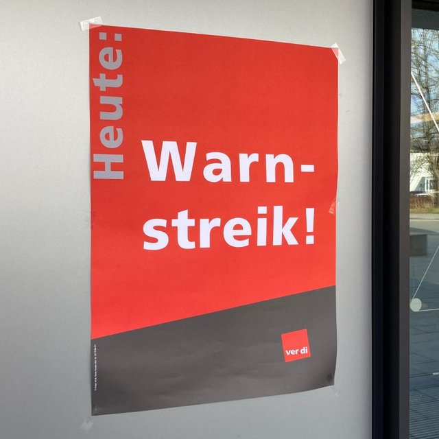Warnstreik!" und darunter befindet sich ein Logo in rot mit der Aufschrift "ver.di". Im Hintergrund sind Bäume und Gebäude sichtbar.