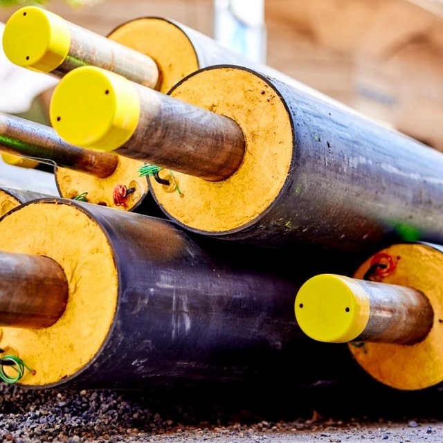 Stapel isolierter Fernwärmerohre mit gelben Endkappen auf einer Baustelle in der Altstadt, sommerliches Licht.