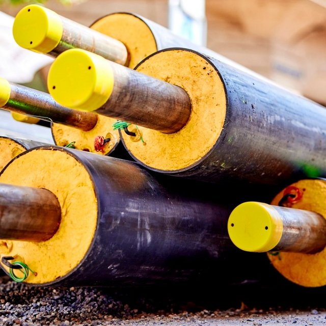Stapel isolierter Fernwärmerohre mit gelben Endkappen auf einer Baustelle in der Altstadt, sommerliches Licht.