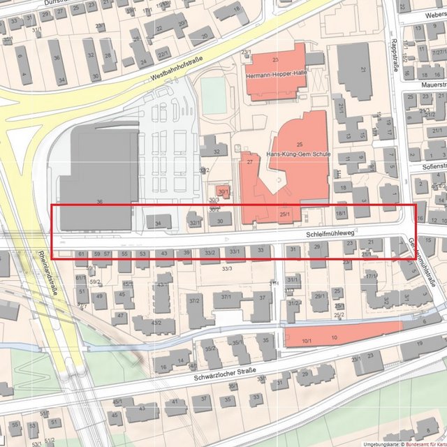 Eine Karte zeigt die Umgebung des Schleifmühlewegs, der zwischen verschiedenen Wohngebäuden verläuft. Auf der Karte sind mehrere Straßen, Gebäudenummern, und wichtige Punkte wie die Hermann-Hepper-Halle und die Hans-Küng-Gemeinschaftsschule eingezeichnet. Die Karte verwendet ein farbcodiertes System, um verschiedene Gebäudetypen und -funktionen darzustellen.